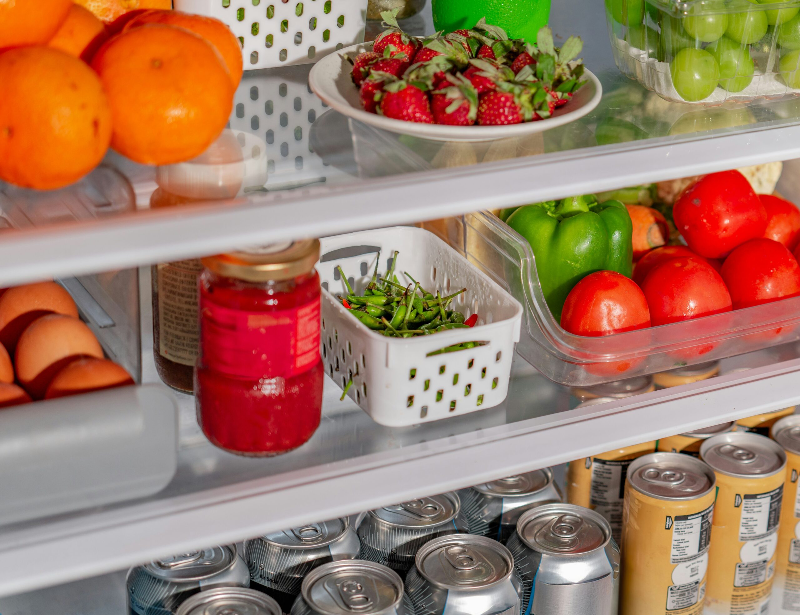 Interior de uma geladeira limpa e iluminada, com alimentos e bebidas perfeitamente dispostos dentro de vários organizadores de acrílico transparentes nas prateleiras.