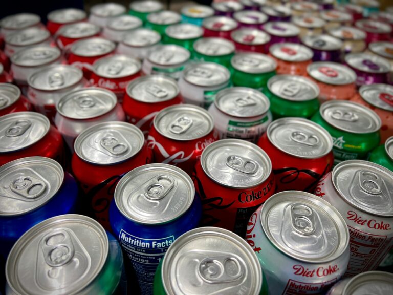 Diversas latas de bebidas de diferentes cores e marcas agrupadas juntas e bem alinhadas sobre uma superfície clara.