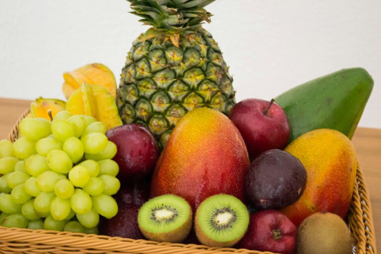 Cesta de vime cheia de frutas variadas e frescas disposta sobre uma mesa iluminada.