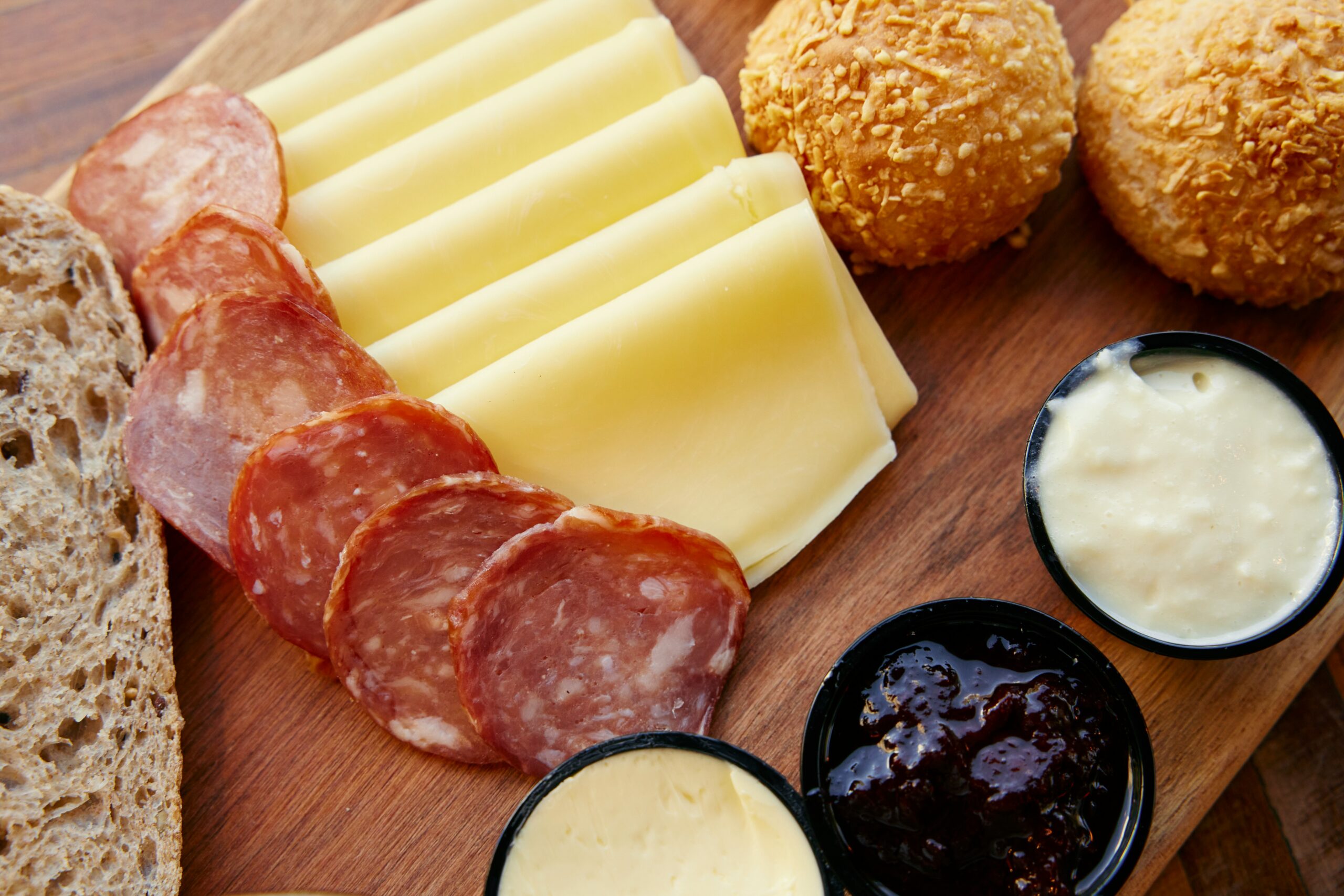 Tábua de madeira servida com fatias de queijo, presunto e salame organizados para aperitivo sobre uma superfície rústica.