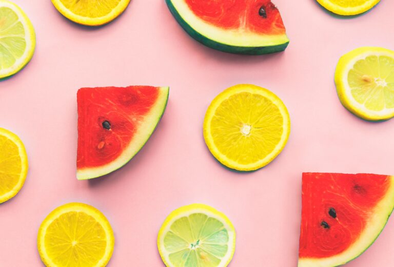 Uma fruteira cheia de frutas variadas em destaque sobre um fundo rosa.