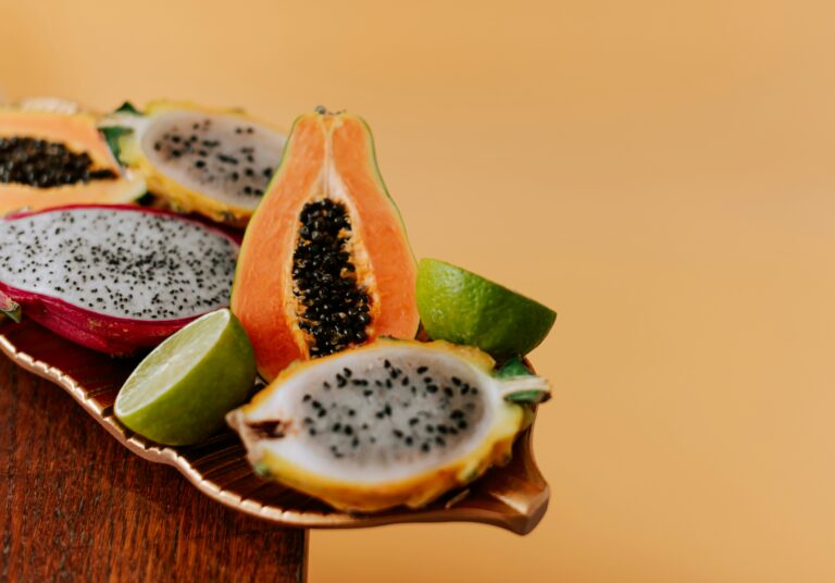 Uma fruteira cheia de frutas variadas em destaque sobre um fundo laranja vibrante.