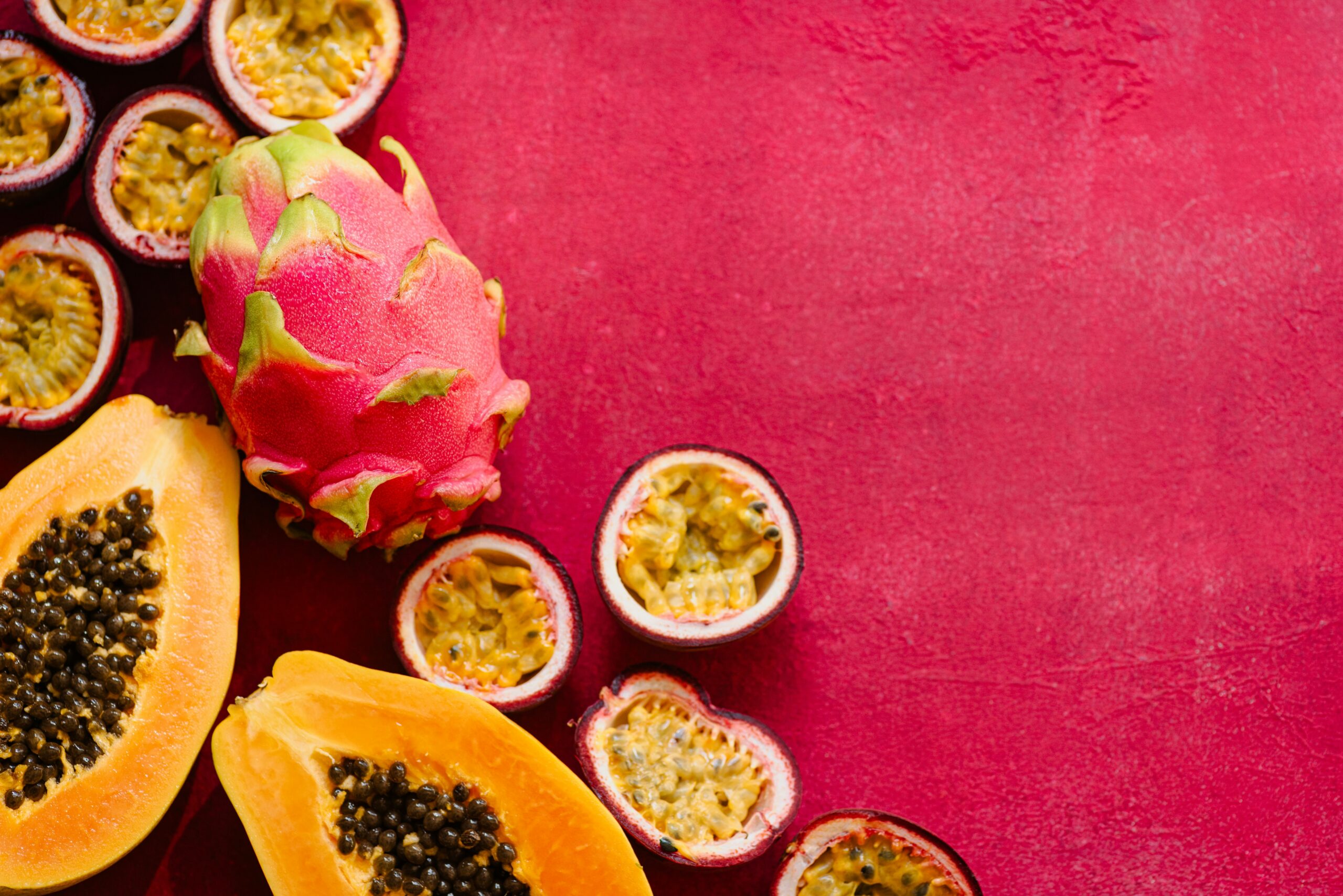 Uma fruteira cheia de frutas variadas em destaque sobre um fundo rosa avermelhado.